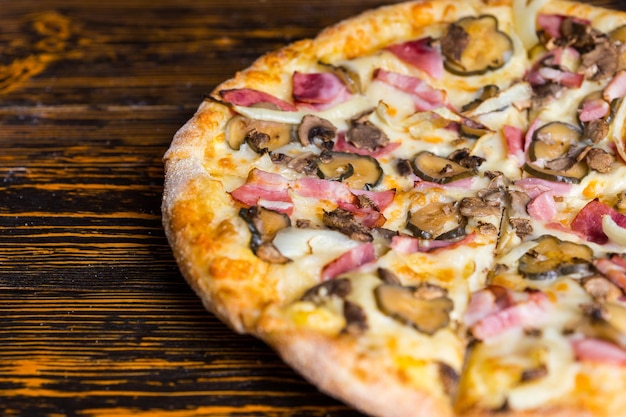 Close up of pizza with ham, mushrooms, onion and pickles on wooden table