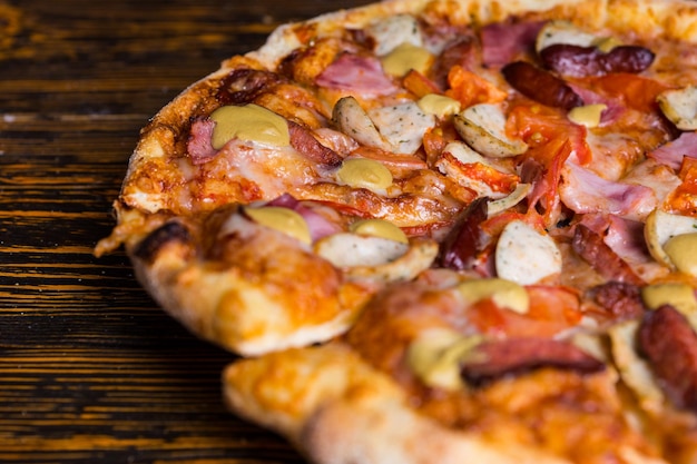 Close up of pizza with ham, sausages and mustard on wooden table