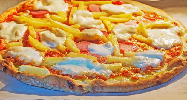 Close up of a pizza with sausage and french fries in the oven