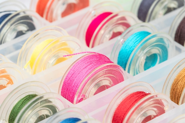 Close up plastic sewing machine bobbins with colourful thread in plastic box.