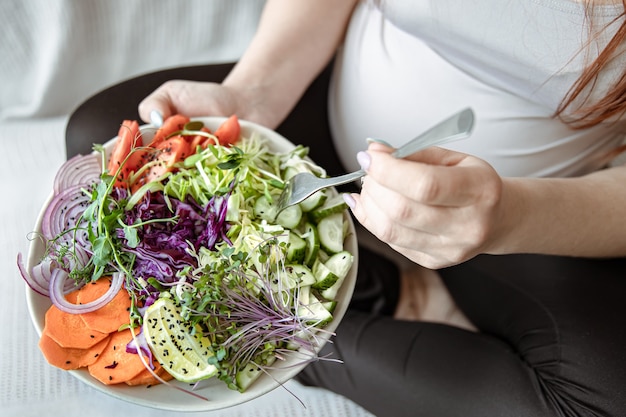 妊娠中の女性の手に新鮮な野菜の明るいサラダとプレートのクローズアップ。