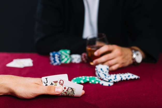 Close-up of a player's hand with playing card on red poker table