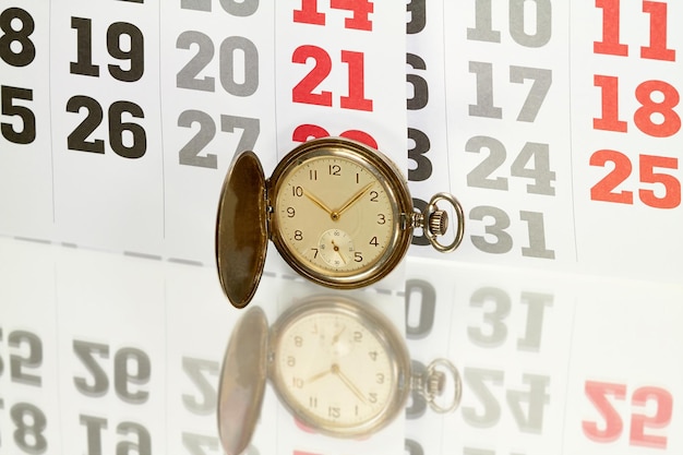 Foto close-up di un orologio da tasca contro un calendario su un tavolo di vetro