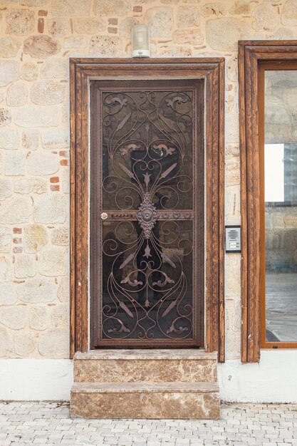 Close-up of a porch with a brown door with a beautiful forged lattice in an old stone mansion house