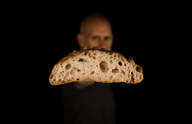 Foto ritratto da vicino di un uomo adulto che tiene un pane tagliato a metà su uno sfondo nero