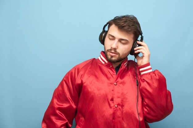 Close-up portrait of an adult man listens to music in headphones with closed eyes on blue