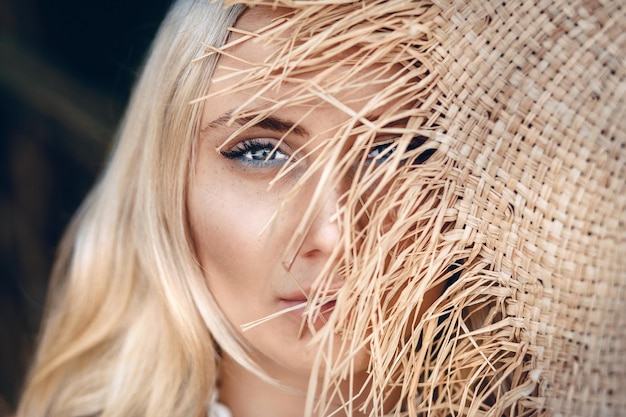 Close up portrait of an amazing blond girl with beautiful blue eyes and a straw hat half covered half of her face