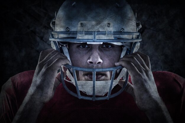 Close-up portrait of American football player holding helmet against dark background