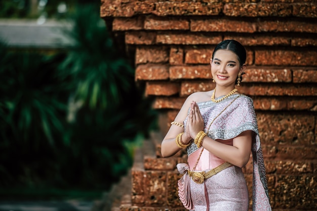 Primo piano, ritratto di una donna affascinante asiatica che indossa un bellissimo abito tipico tailandese in un antico tempio o in un luogo famoso con una posa graziosa