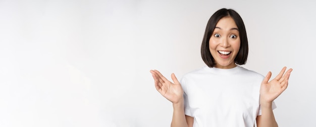 Close up portrait of asian girl looking surprised wow face reacting amazed at smth standing in white