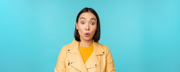 Close up portrait of asian girl looks surprised at amazed wow face expression stands over blue background