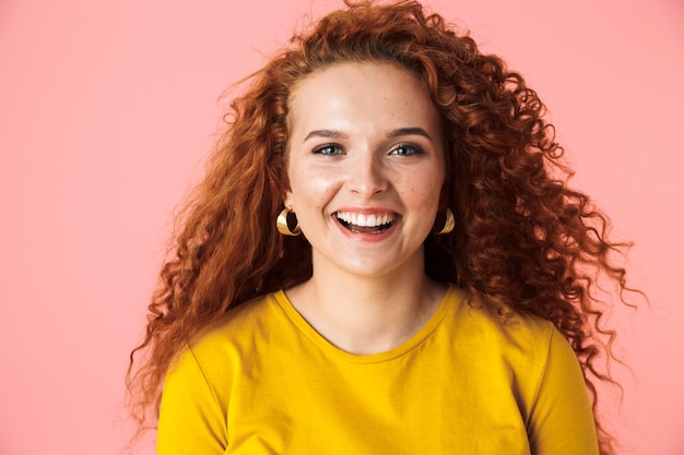 Close up portrait of an attractive cheerful young woman with long curly red hair standing isolated