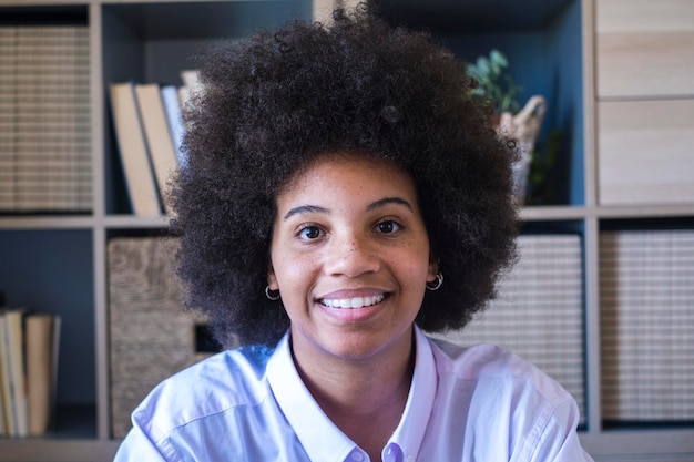 Close-up portrait of attractive dark skinned young woman with curly Afro hairstyle. African american businesswoman smiling at office. Young positive lady smiling and looking at camera