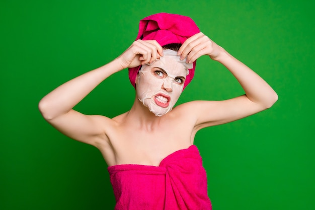 Close-up portrait of attractive desperate mad irritated lady wearing turban applying unpleasant facial mask isolated on vivid green color background