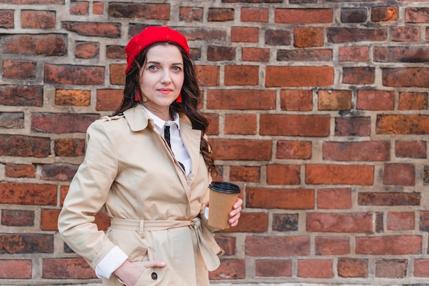 Close-up portrait of attractive pretty stylish cheerful curly-haired brunette girl holding at paper-cup coffee isolated on red brick, Happy woman walking outdoors.