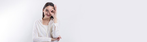 Close up portrait of attractive quirky young woman making binoculars with hands showing ok gesture on white studio background