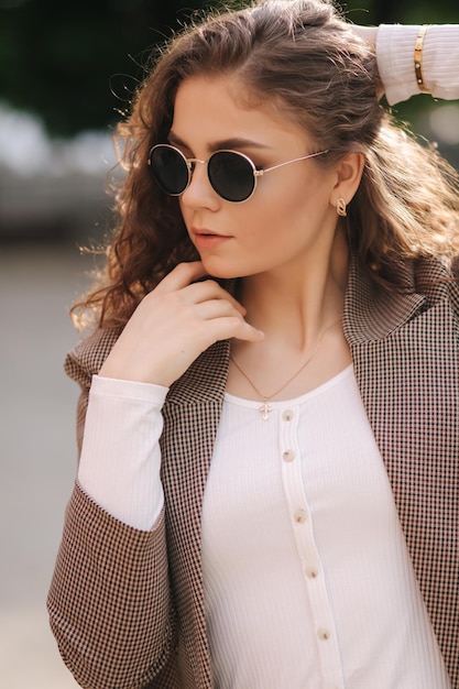 Крупным планом Портрет привлекательной женщины с вьющимися волосами в солнцезащитных очках на улице Красивая молодая модель в городе