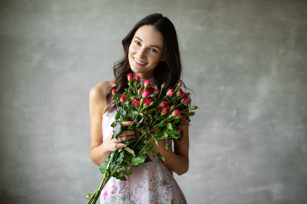 Close-up portrait of attractive young woman in summer dress holding bouquet of roses