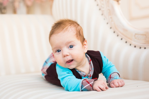 Close-up portrait of baby boy with red hair and blue eyes. Newborn child lyling in couch.