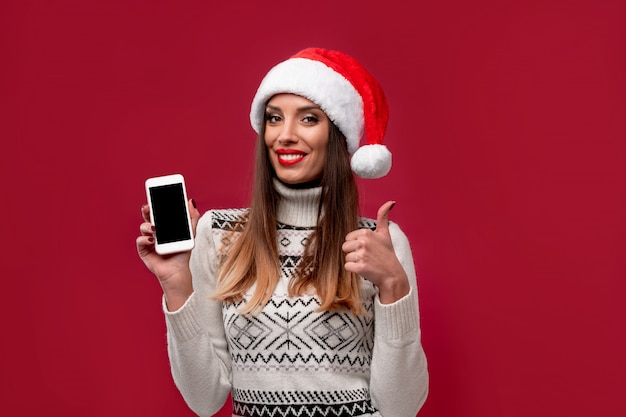 Close up portrait beautifiul caucasian woman in red Santa hat on red  wall. Christmas New Year  concept. Cute woman teeth smiling positive emotions with free copy space