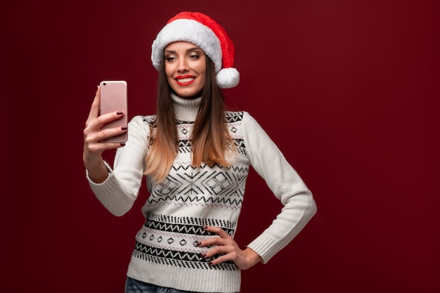 Close up portrait beautifiul caucasian woman in red Santa hat on red  wall. Christmas New Year  concept. Cute woman teeth smiling positive emotions with free copy space