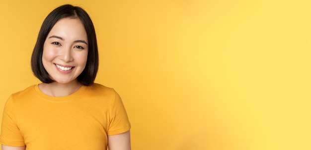 Photo close up portrait of beautiful asian woman smiling looking cute and tender standing against yellow b