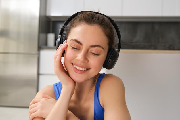 Close up portrait of beautiful brunette girl in sportswear sits in wireless headphones and listens