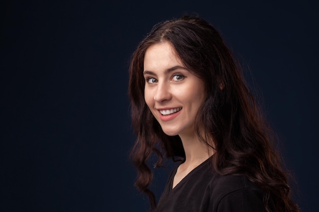 Close-up portrait of a beautiful brunette with curly hair and professional make-up posing on a black background.