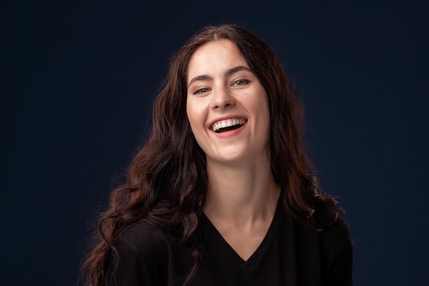 Close-up portrait of a beautiful brunette with curly hair and professional make-up posing on a black background.