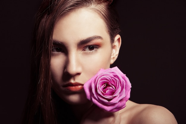 Close-up portrait of beautiful brunette woman with pink rose