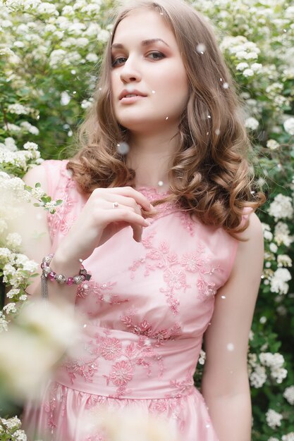Close up portrait of a beautiful girl in a pink vintage dress standing near white flowers