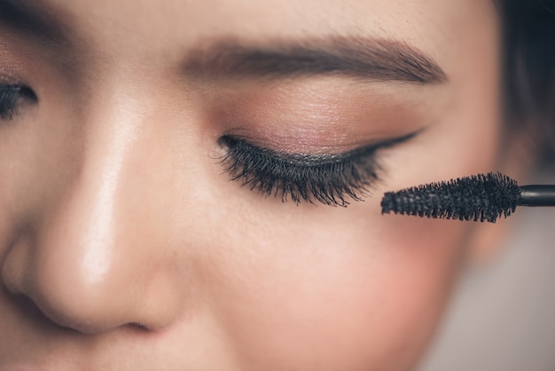 Close-up portrait of beautiful girl touching black mascara to her lashes