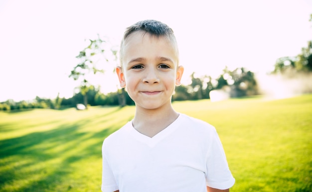 Close up portrait of beautiful happy and funny little boy or kid outdoors in green summer park