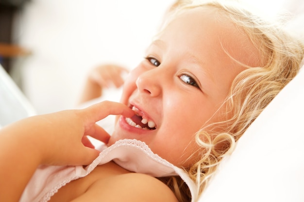 Foto chiuda sul ritratto di bella bambina che si trova sul letto e sul sorridere