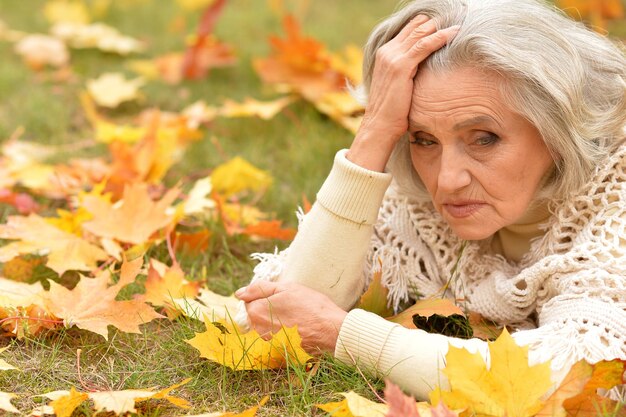 Close up portrait of beautiful sad senior woman on blurred autumn background