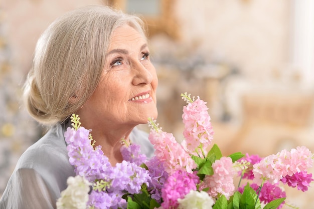 Close up portrait of beautiful senior woman posing at home with flowers