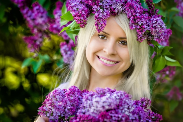 Close Up portrait beautiful smiling young blonde woman is wearing wreath of lilac flowers