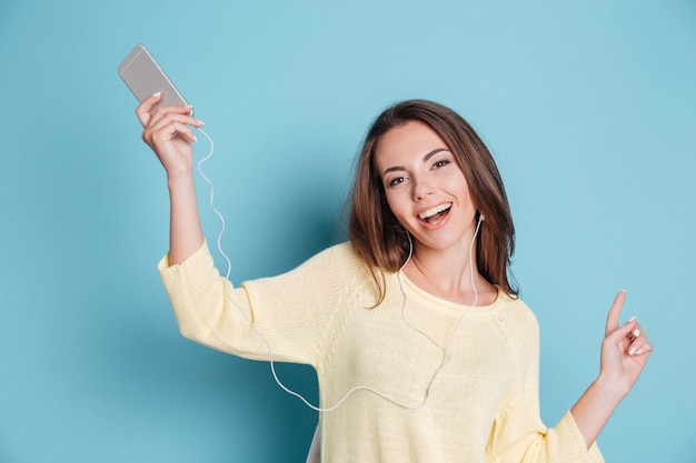 Close-up portrait of a beautiful smiling young woman listening music and sitting on the chair isolated on a blue background