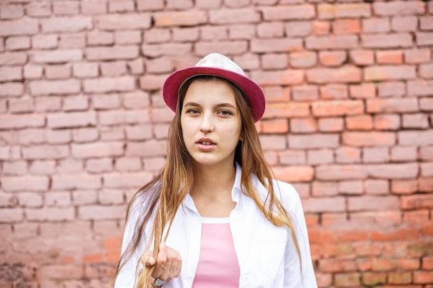 Foto ritratto ravvicinato di una bella ragazza alla moda con cappello vicino al muro di mattoni rosa come sfondo