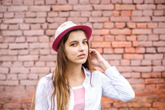Close up portrait of beautiful stylish kid girl in hat near pink brick wall as background