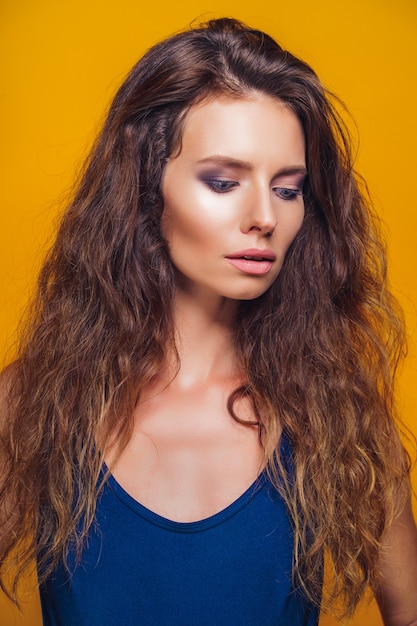 Close-up portrait of a beautiful tanned young woman with curly hair on yellow background.