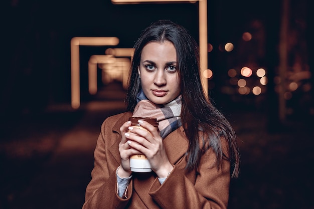 클로즈업 초상화 베이지색 코트와 스카프를 착용하고 커피 한 잔을 들고 있는 아름다운 여성