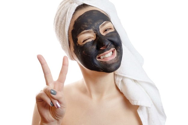 Close-up portrait beautiful woman with facial black mask on white background, girl with a white towel on her head