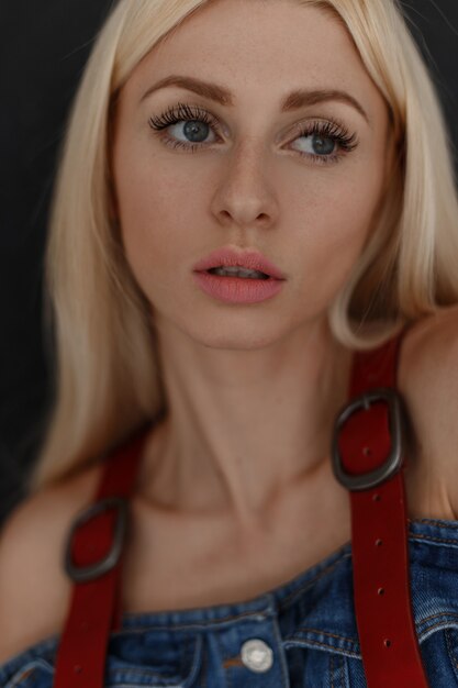 Photo close-up portrait of a beautiful young attractive woman with freckles in fashionable denim clothes on a black wall.