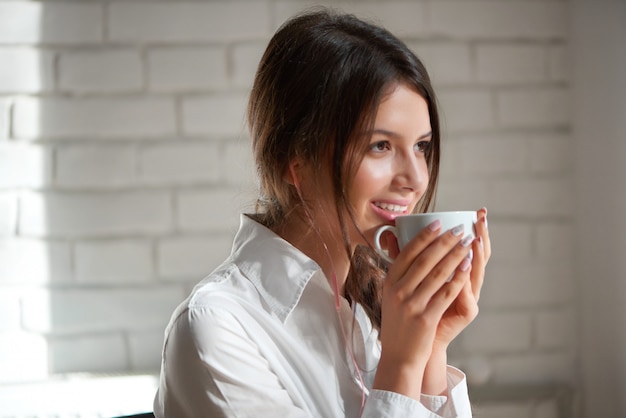 Close up portrait of a beautiful young dark haired woman smiling happily enjoying her morning cup of coffee looking away positivity beauty lifestyle relax leisure urban living youth recreation.