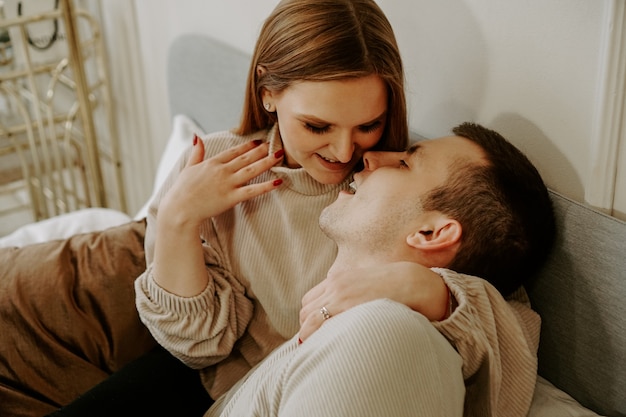 Close-up portrait of a beautiful young kissing couple in bed at home. Soft colors