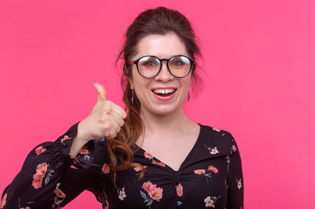Close-up portrait of a beautiful young positive female student with glasses showing thumb up posing