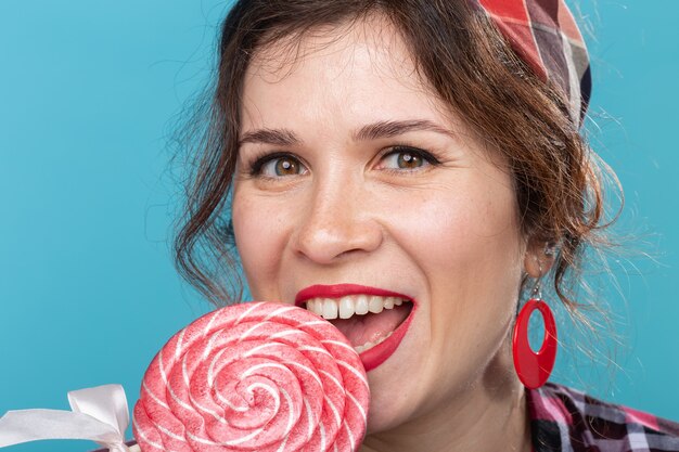 Photo close up portrait of beautiful young woman eating lollipop over blue surface