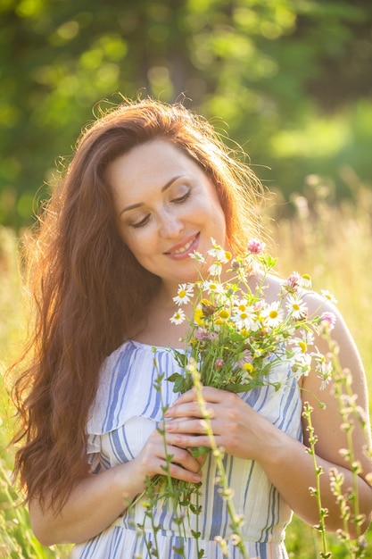 화창한 여름에 아름다운 야생화의 꽃다발을 스니핑하는 아름 다운 젊은 여자의 클로즈 업 초상화