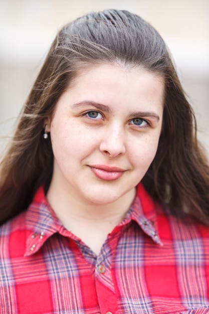 Close up portrait of big plus size beautiful stylish kid girl with leather jacket and red plaid shirt near brick building in urban street as background